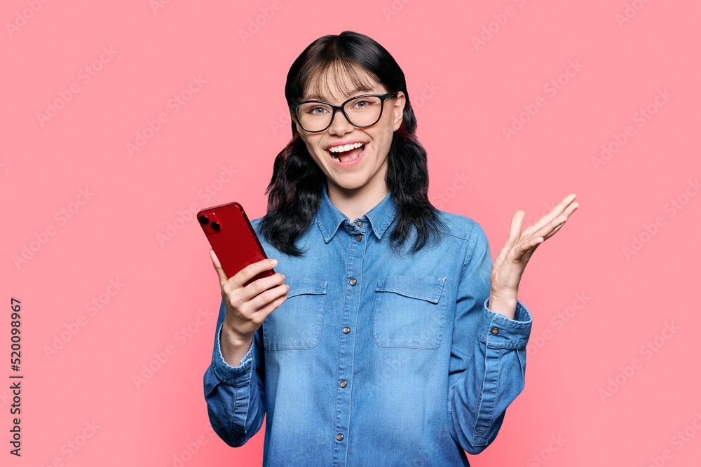 Naklejka premium Surprised teenage girl looking at smartphone screen on pink background