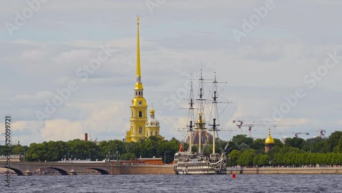 Colorful landscape of the green embankment of St. Petersburg near the Trinity Bridge with the Peter and Paul Fortress and an ancient frigate, the golden dome of the chapel on a clear sunny day