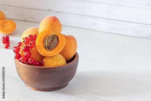 apricots and red currants in a wooden bowl on a white wooden background, apricot cut in half, fresh fruits and berries, copy space
