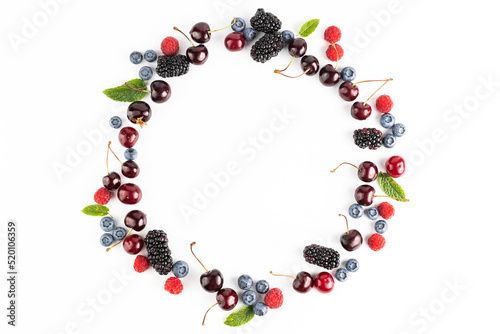 Cherries, blueberries, blackberries, raspberries and mint leaves are arranged in a circle on a white background. View from above.