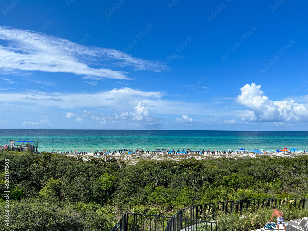 Fototapeta premium An aerial view of the Beach with Blue Umbrella and Lounge Chairs lined up at the Watercolor Community Club in Watercolor, Florida.