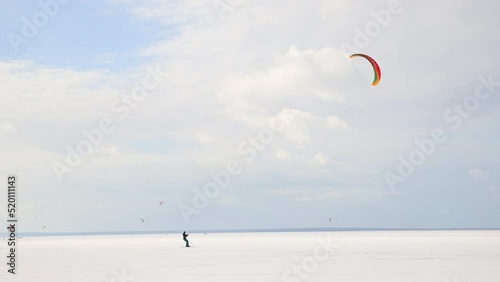Minimalism scenic view of adult man enjoy extreme sport activities riding kite surfing board on white desert snow frozen lake surface against blue sky. Winter outdoors adventure lifestyle