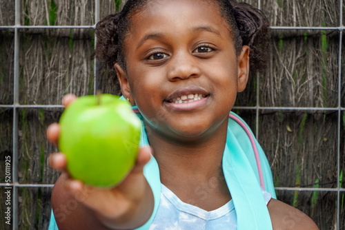 afroamerican school girl with backpack  eating green apple. Daily rate of fruit for children.