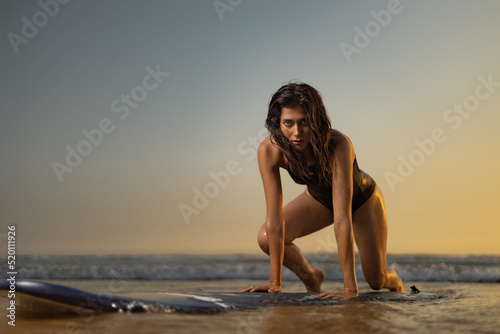 Surfing training. Surf lessons. Girl with surf board ready to surfing. Woman surfer on the surfboard on a beach at sunset. © Mike Orlov