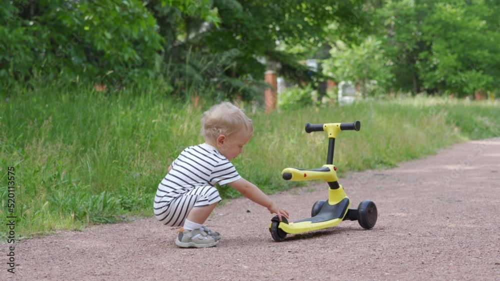Happy kid having fun learning to ride a balance bike for younger kids outdoors, 1.5 year old child playing with kick scooter for toddlers in the park in summer. Happy kid having fun learning to ride a balance bike for younger kids outdoors, 1.5 year old child playing with kick scooter for toddlers in the park in summer.