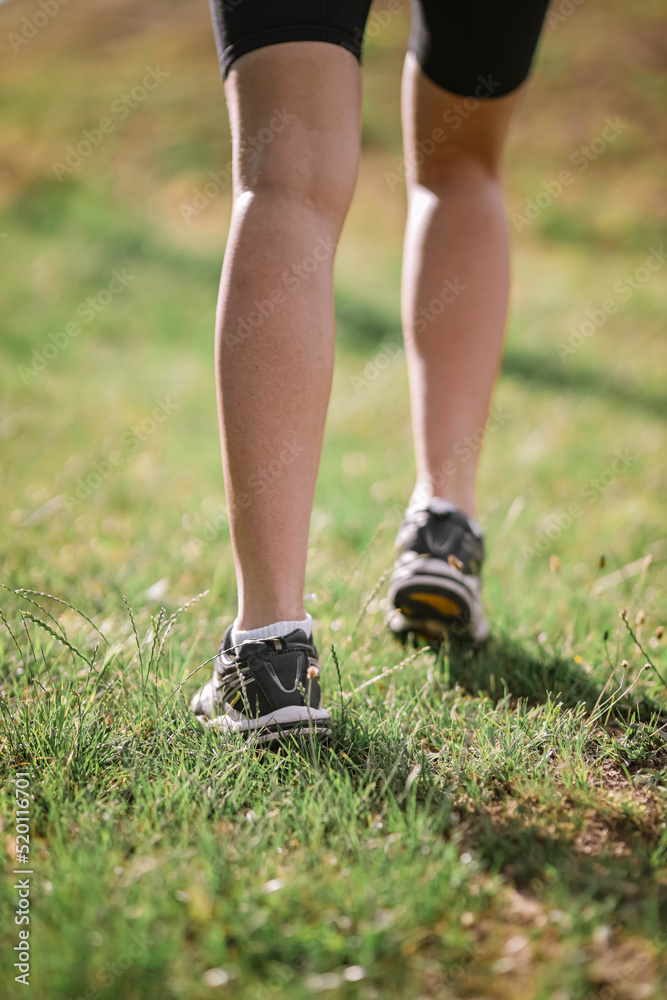 Closeup photo of athlete girl's legs dressed in sportswear with sneakers going up in mountains on summer green grass. Happy young female sport, workout, travelling, ecology, healthy lifestyle concept Closeup photo of athlete girl's legs dressed in sportswear with sneakers going up in mountains on summer green grass. Happy young female sport, workout, travelling, ecology, healthy lifestyle concept