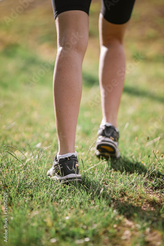 Closeup photo of athlete girl's legs dressed in sportswear with sneakers going up in mountains on summer green grass. Happy young female sport, workout, travelling, ecology, healthy lifestyle concept