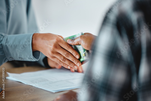 Illegal, suspicious payment and bribery in an office with documents on the table. Closeup of two business people hands exchanging a cash payment in a corporate office, committing crime or fraud photo