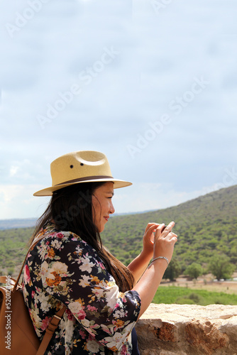 Single Latin adult woman with hat uses her travel cell phone to stay connected, take photos, selfies, video calls, locate herself on the map to share experiences  © Arlette