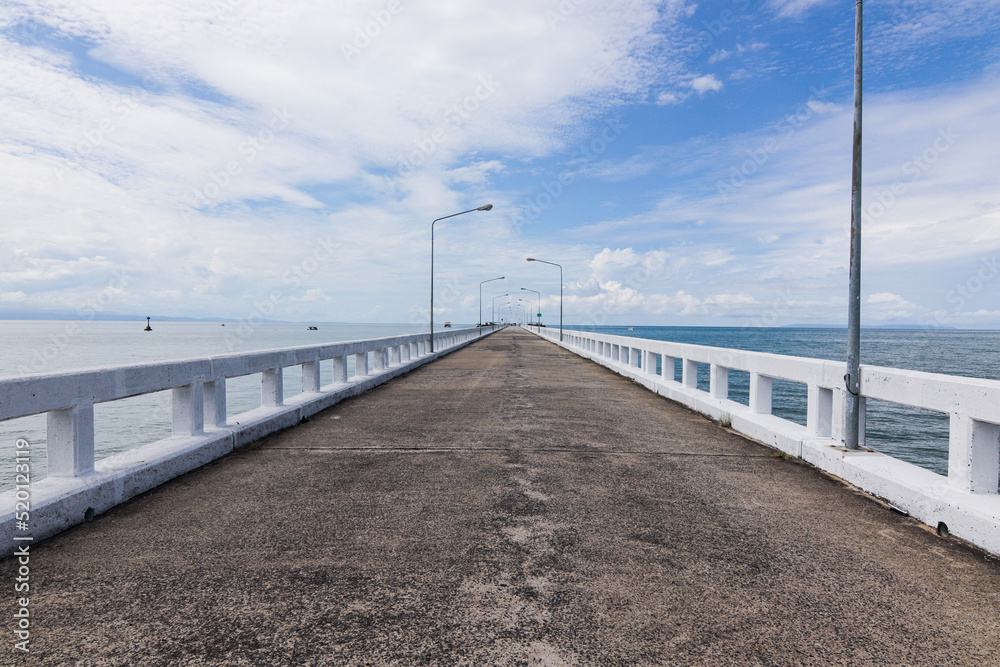 Long jetty bridge overlooking bright blue sky and high floating clouds in sea view background picture.