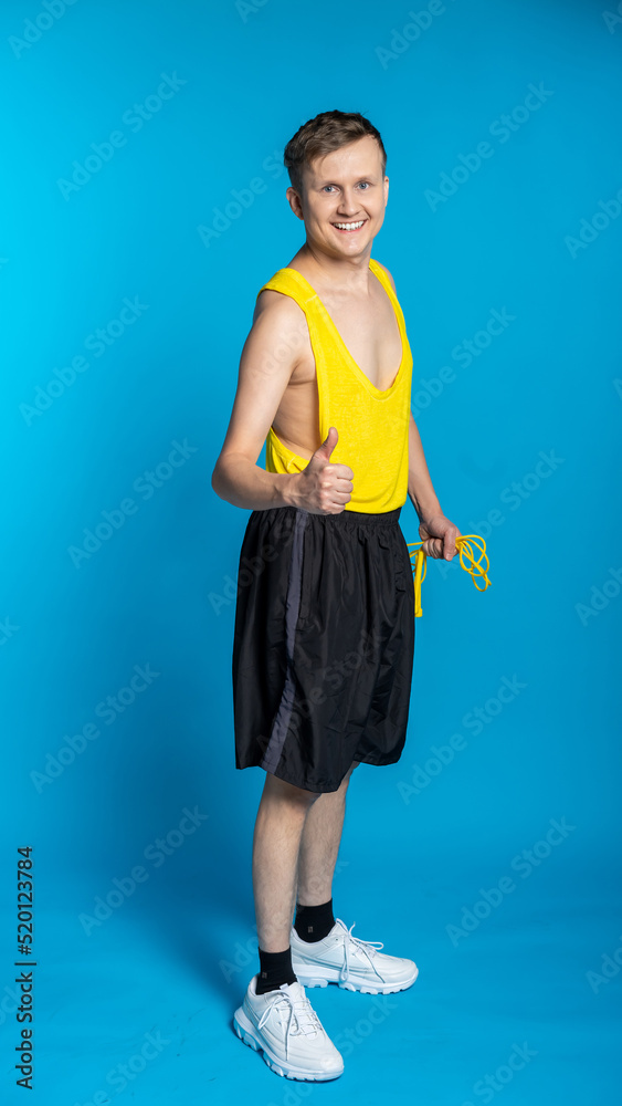 lean sportsman in a yellow t-shirt and black shorts on a blue background. funny sportsman with a skipping rope in training lean sportsman in a yellow t-shirt and black shorts on a blue background. funny sportsman with a skipping rope in training