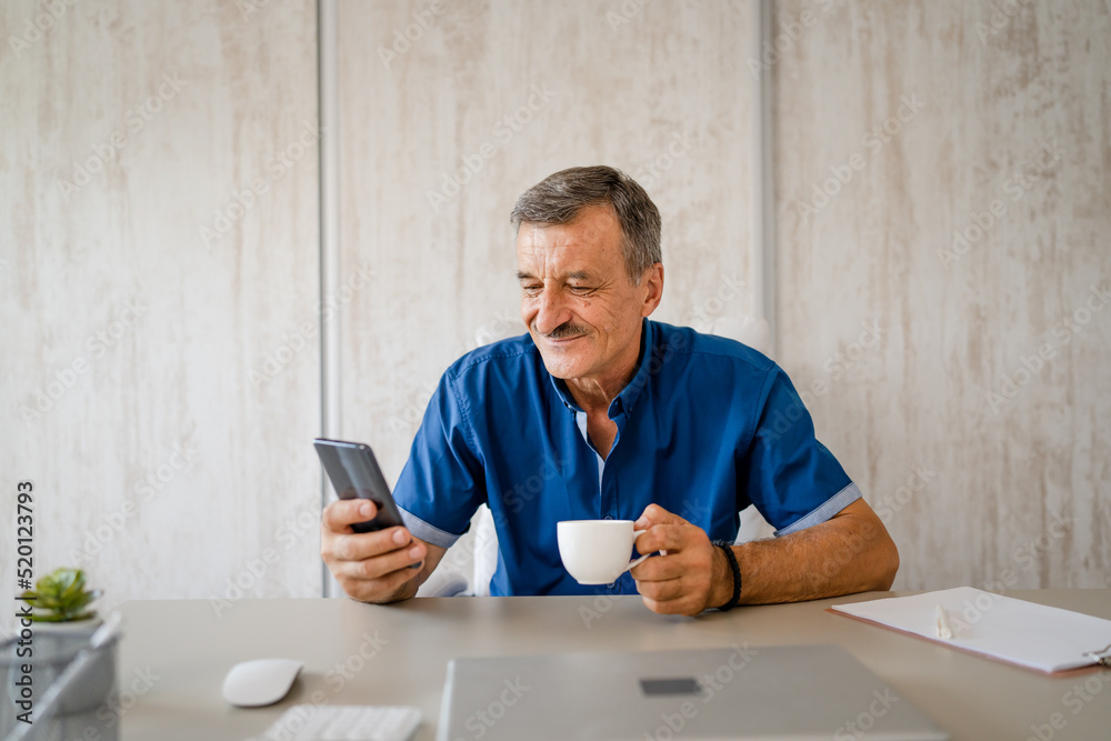 senior man hold cup of coffee and mobile phone while sitting at work senior man hold cup of coffee and mobile phone while sitting at work