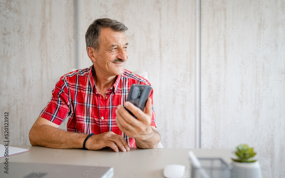senior man hold cup of coffee and mobile phone while sitting at work senior man hold cup of coffee and mobile phone while sitting at work