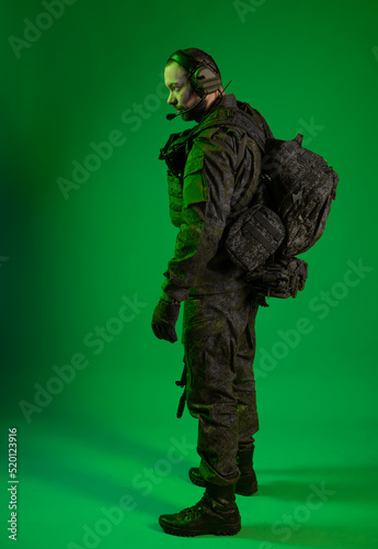 soldier in the studio on a green background with colored light. a man in military uniform with a gun, rifle or machine gun. military. airball player