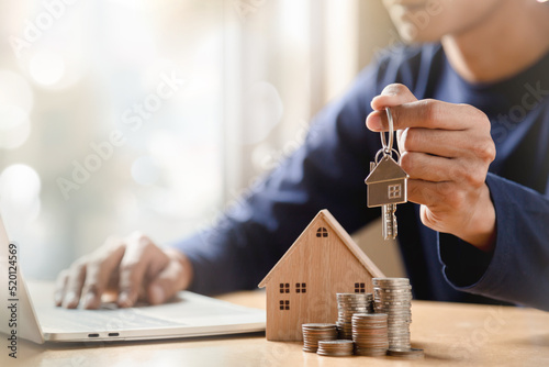 Businessman choosing mini wood house model from model and row of coin money on wood table, selective focus, Planning to buy property. Choose what's the best. 