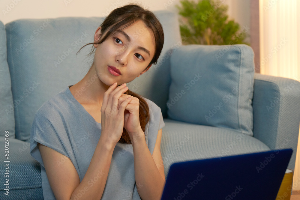 夜にリビングでパソコンの前で考える女性 夜にリビングでパソコンの前で考える女性