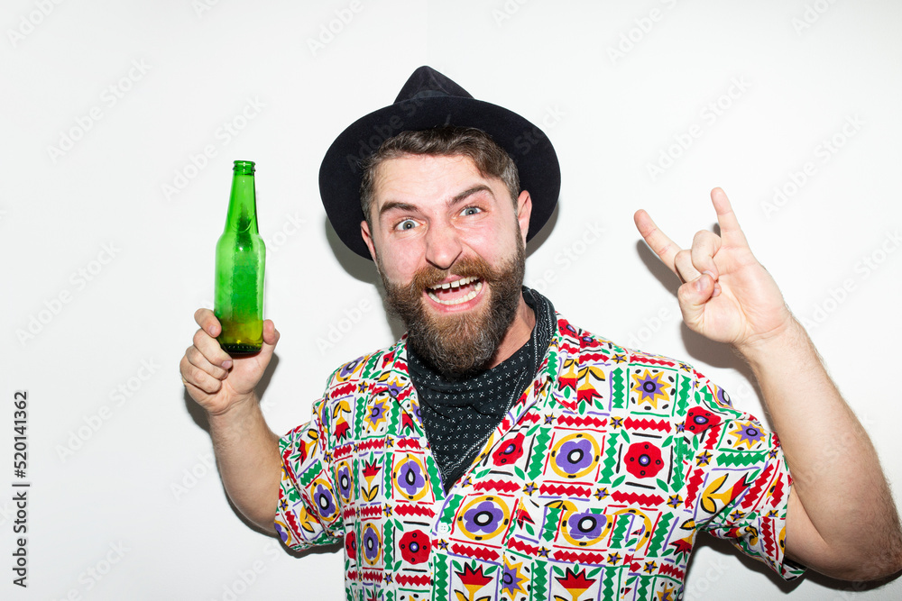Funny young man in hat holding glass bottle and looking at camera isolated on white background, showing horn sign. Funny young man in hat holding glass bottle and looking at camera isolated on white background, showing horn sign.