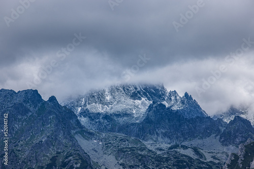 Tatras high mountain pass in dramatic atmosphere. Overcast cloudscape with snowy mountain peak. Abstract high mountain cloudy sky background, travel adventure. Extreme hiking, recreational scenic