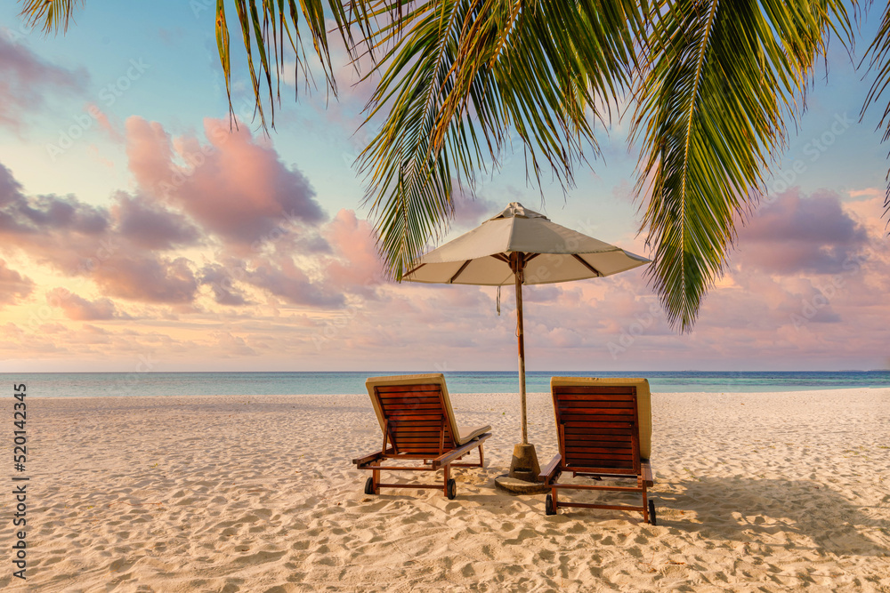 Beautiful tropical sunset shore, couple sun beds or chairs, umbrella under palm leaves. Sea sand colorful twilight sky. Romantic relax lifestyle inspire island beach background. Summer travel vacation