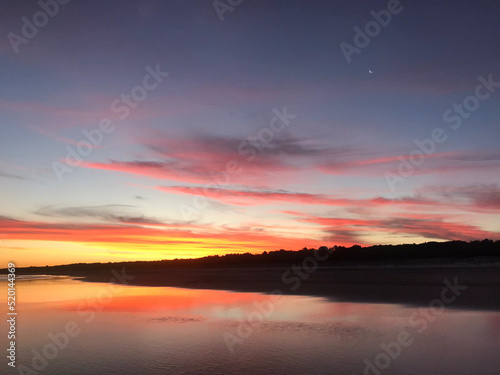 Long shot of beautiful evening sunset with pink clouds on tranquil beach, sunset reflected on wet sand.