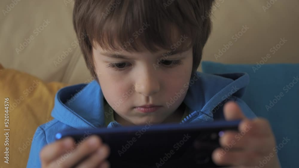 Child Playing Games In Phone at Home Sitting on Couch. Boy Playing Video Game on Mobile Phone. Preschooler Plays Video Game Smartphone on Sofa. Kid Using Phone for Gaming Online Education Social Media Child Playing Games In Phone at Home Sitting on Couch. Boy Playing Video Game on Mobile Phone. Preschooler Plays Video Game Smartphone on Sofa. Kid Using Phone for Gaming Online Education Social Media