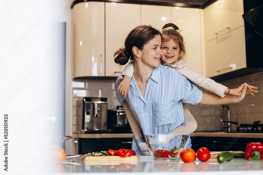 Mother with little daughter cooking at the kitchen and having fun