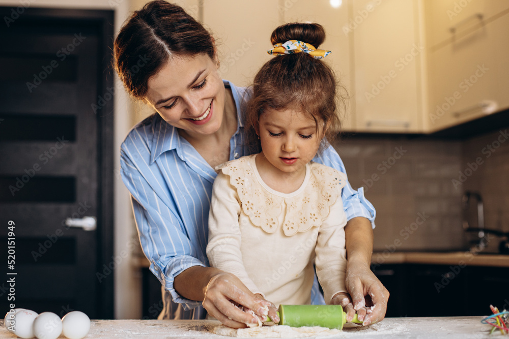 Fototapeta premium Mother with daughter preparing dough using rolling pan at the kitchen