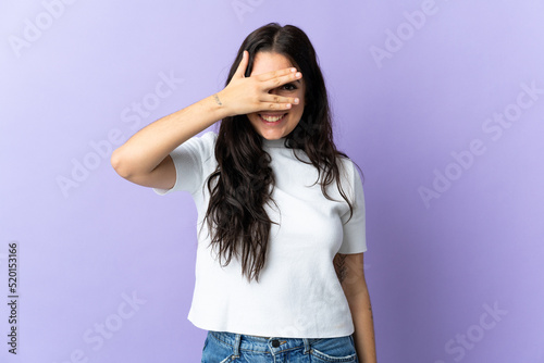 Young caucasian woman isolated on purple background covering eyes by hands and smiling