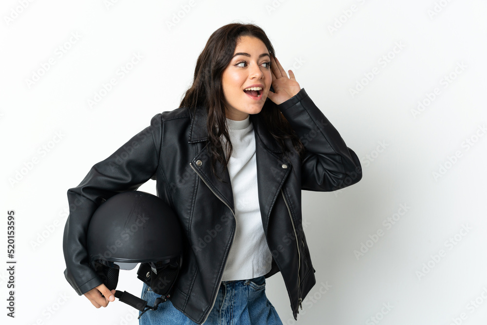 Woman holding a motorcycle helmet isolated on white background listening to something by putting hand on the ear Woman holding a motorcycle helmet isolated on white background listening to something by putting hand on the ear