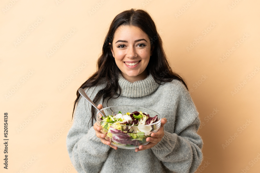 Young caucasian woman isolated on beige background holding a bowl of salad with happy expression