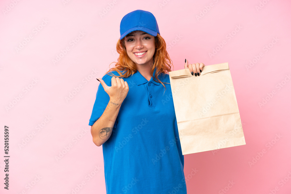 Young caucasian woman taking a bag of takeaway food isolated on pink background pointing to the side to present a product Young caucasian woman taking a bag of takeaway food isolated on pink background pointing to the side to present a product