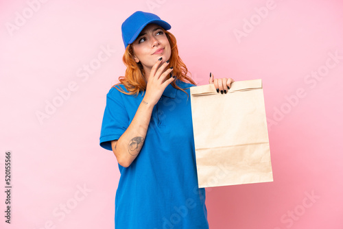 Young caucasian woman taking a bag of takeaway food isolated on pink background and looking up