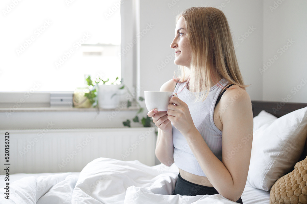 Young beautiful blonde 30s woman having breakfast in bed with coffee in cozy bedroom. Morning rituals. Young beautiful blonde 30s woman having breakfast in bed with coffee in cozy bedroom. Morning rituals.