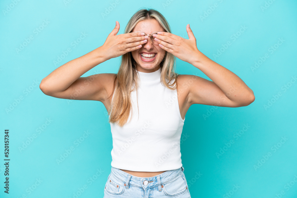 Young caucasian woman isolated on blue background covering eyes by hands and smiling Young caucasian woman isolated on blue background covering eyes by hands and smiling