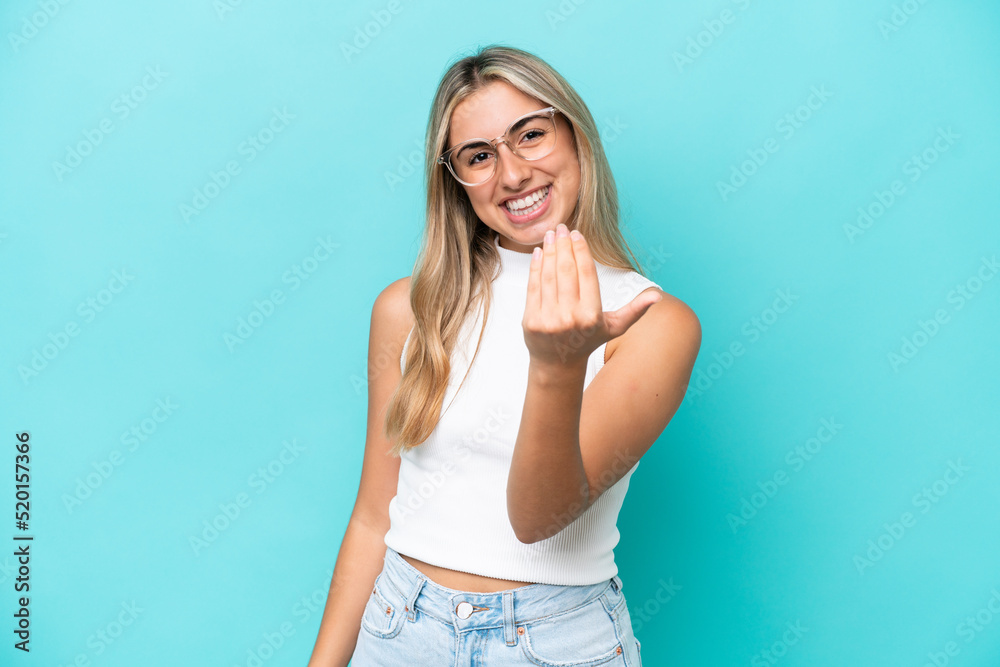 Young caucasian woman isolated on blue background inviting to come with hand. Happy that you came Young caucasian woman isolated on blue background inviting to come with hand. Happy that you came