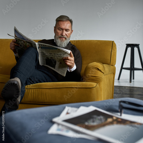 Grey hair caucasian man reading newspaper on sofa
