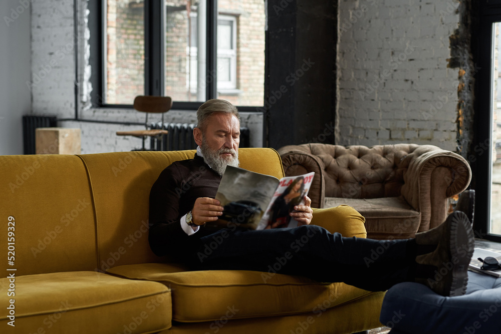Elderly focused man read journal on sofa at home Elderly focused man read journal on sofa at home