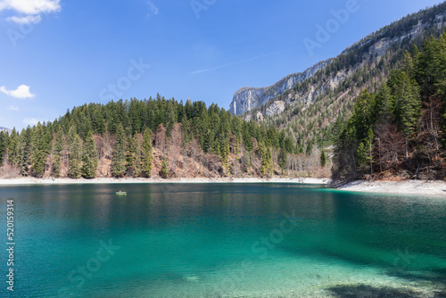 Panorama of emerald waters of the alpine lake Tovel framed by forest and rocks under clear blue spring sky, Ville d'Anaunia, Trentino, Italy