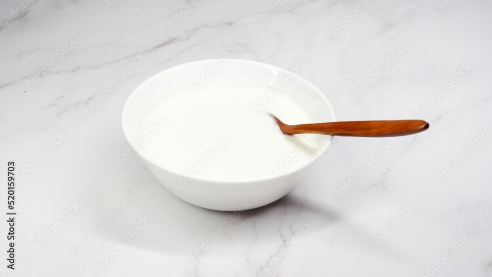 Plain yogurt in a white bowl served with a wooden spoon Plain yogurt in a white bowl served with a wooden spoon