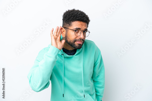 Young Brazilian man isolated on white background listening to something by putting hand on the ear