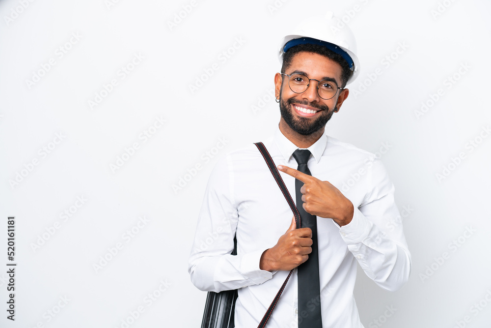 Young architect Brazilian man with helmet and holding blueprints isolated on white background pointing to the side to present a product Young architect Brazilian man with helmet and holding blueprints isolated on white background pointing to the side to present a product