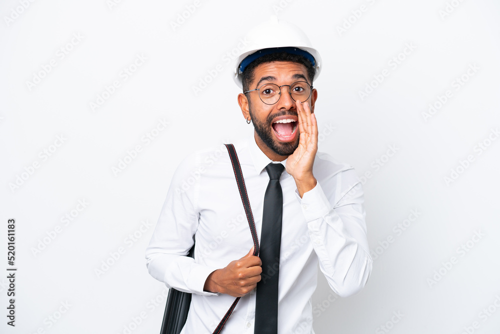 Young architect Brazilian man with helmet and holding blueprints isolated on white background shouting with mouth wide open Young architect Brazilian man with helmet and holding blueprints isolated on white background shouting with mouth wide open