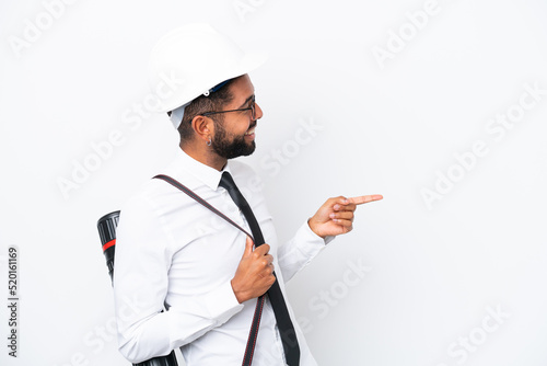 Young architect Brazilian man with helmet and holding blueprints isolated on white background pointing finger to the side and presenting a product