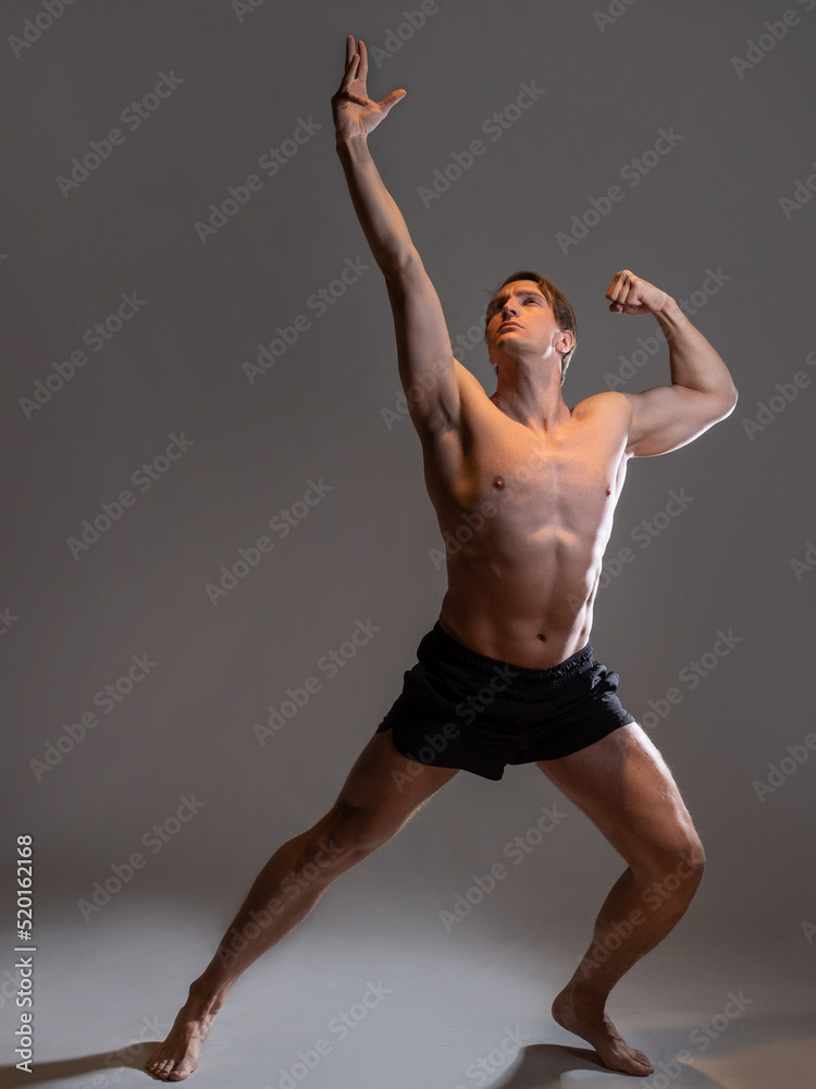 Obraz premium young muscular man in an expressive pose, artistic pose of the hero with outstretched arms. Beautiful muscles. extraordinary athletic body. Portrait on a gray background