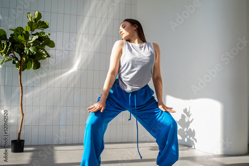 Modern dance, stylish young brunette in baggy blue pants dancing in jazz-funk style. Stylish and youthful. The dance hall is illuminated by sunlight, bright colors