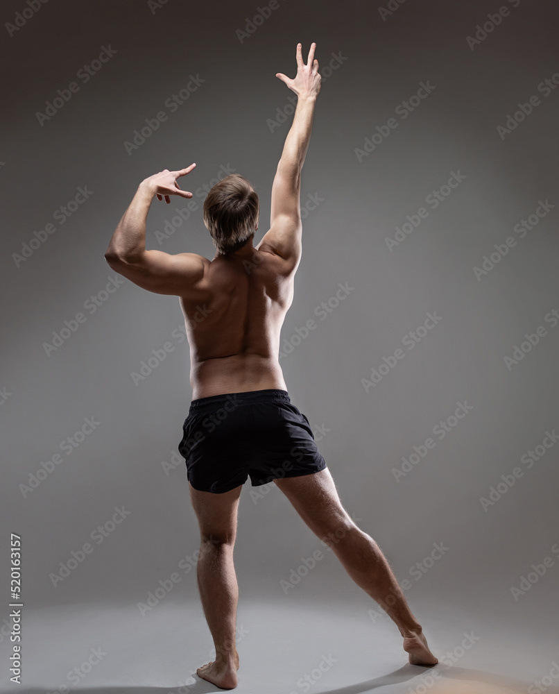young muscular man in an expressive pose, throwing his hands up. Beautiful muscles. extraordinary athletic body. Portrait on a gray background