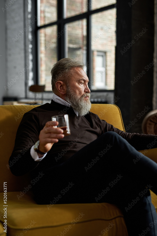 Grey hair man drinking brandy on sofa at home