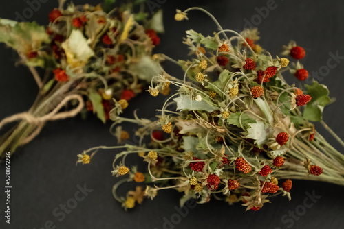 Bunch of dried wild strawberry twigs with berries on dark table surface. Herbal medicine remedy