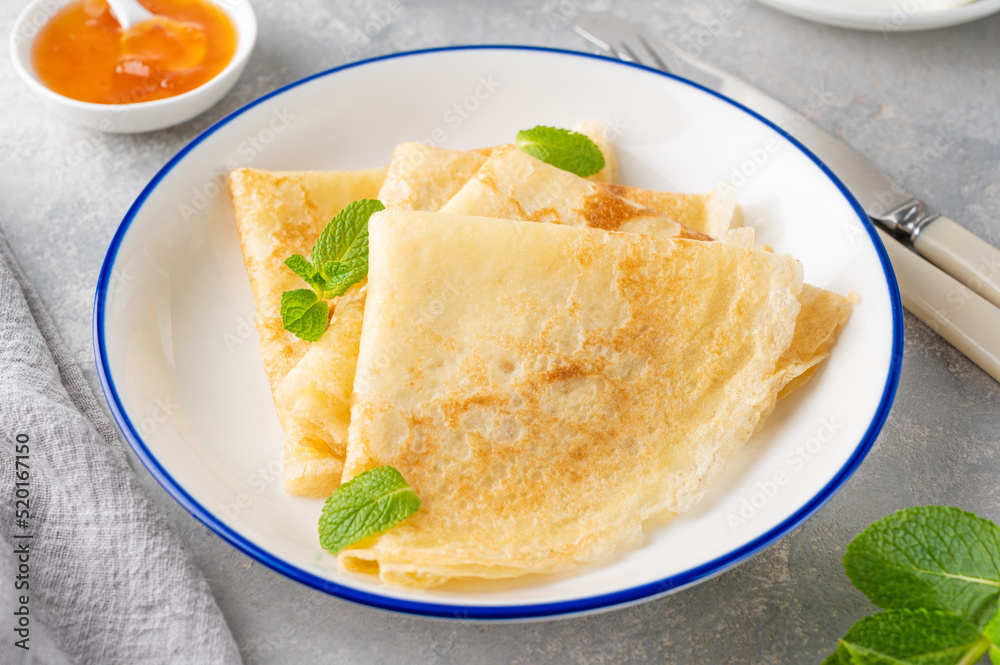 Stack of traditional thin pancakes or crepes on a plate with honey and sour cream on a gray concrete background. Food for Maslenitsa. Copy space Stack of traditional thin pancakes or crepes on a plate with honey and sour cream on a gray concrete background. Food for Maslenitsa. Copy space