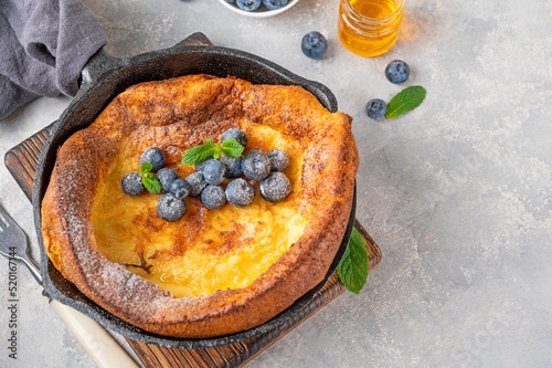 Homemade Dutch Baby pancake with fresh blueberries, mint and sprinkled with icing sugar in iron skillets on a gray concrete background. Copy space. photo